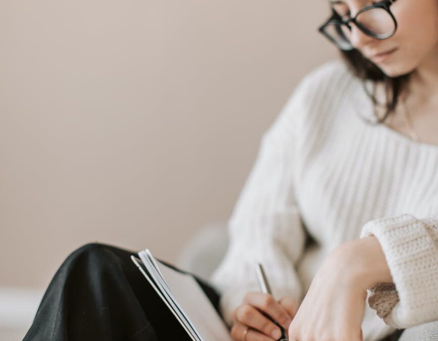 crop young woman writing schedule in diary on sofa
